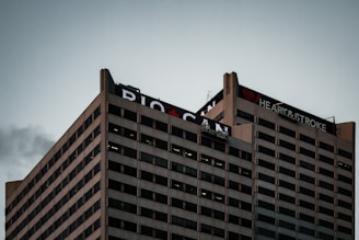 A tall office building with a grid-like pattern of windows is topped with signage that includes the words 'Heart & Stroke' and 'RBC CAN' with a red heart icon. The sky is overcast, creating a subdued atmosphere.