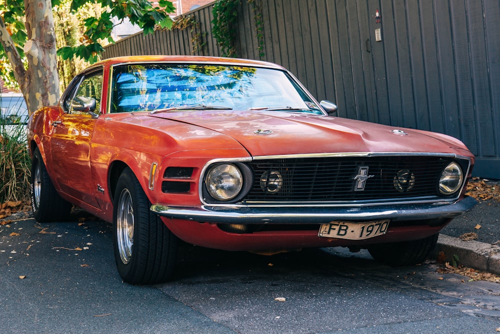 red chevrolet classic car parked near brown wooden fence during daytime