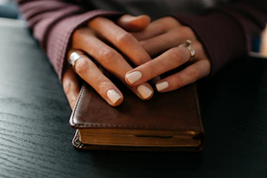 Elegant hands wearing multiple rings with semi-precious stones, holding a vintage book.