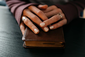 Hands carefully binding a book with deep red earthy cover and black thread stitching.