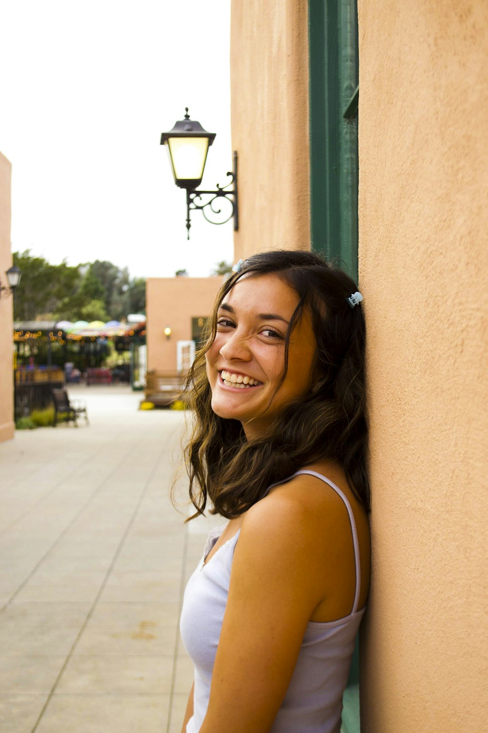 smiling woman in white tank top standing near brown wall during daytime