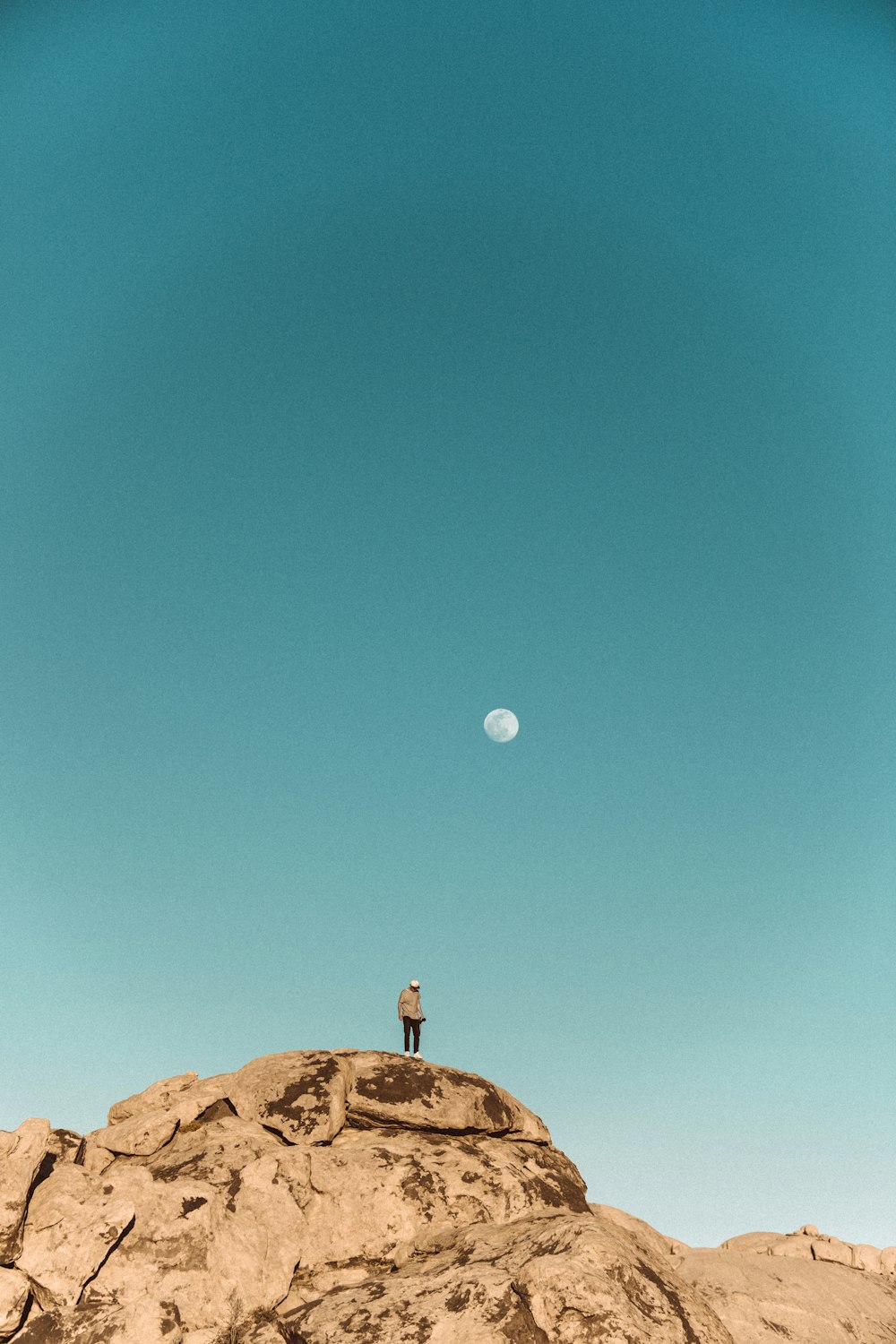 man in brown shirt standing on brown rock under blue sky during daytime