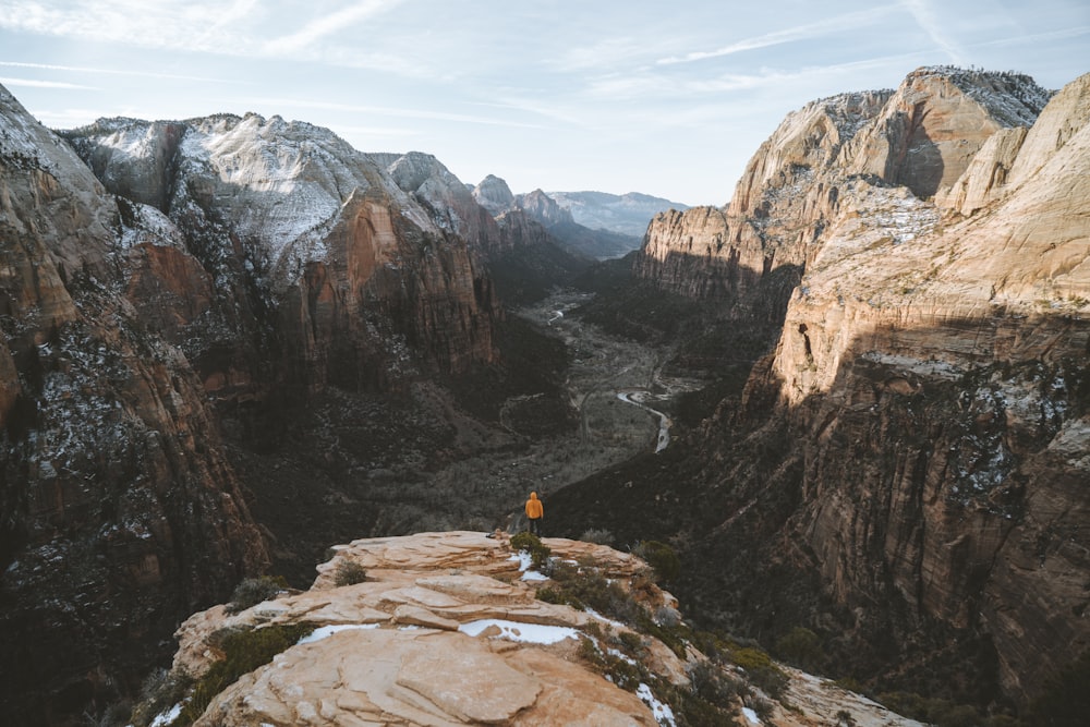 person in yellow jacket sitting on brown rock formation during daytime