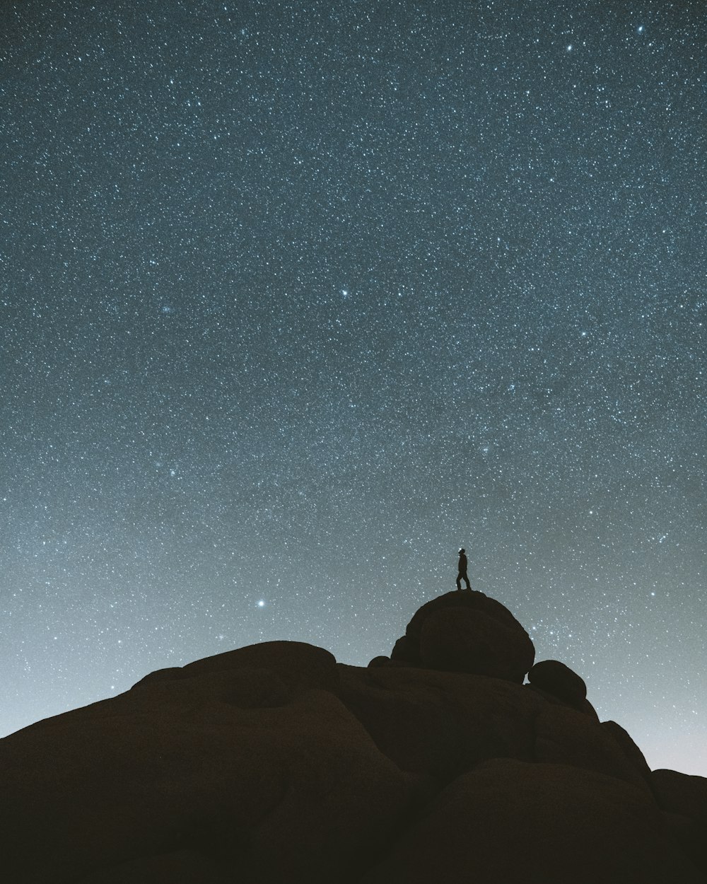 silhouette of person on top of mountain under starry night