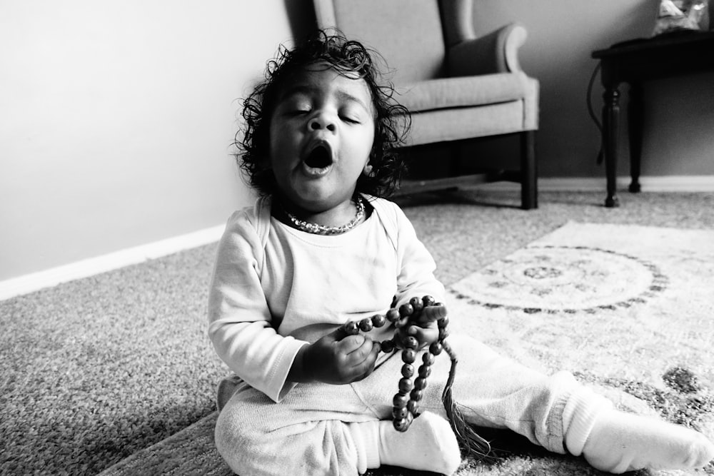 a little girl sitting on the floor with her hands in her mouth
