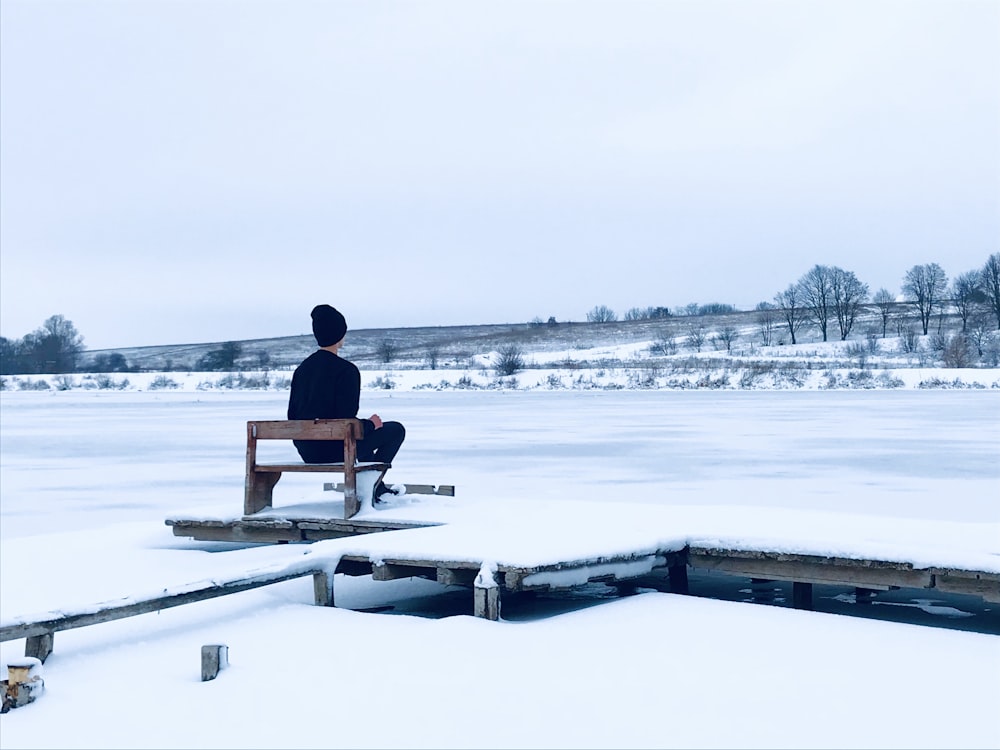 man in red shirt sitting on brown wooden bench on snow covered ground during daytime