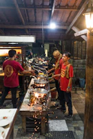 Students smiling as they stir woks filled with colorful ingredients over open flames.