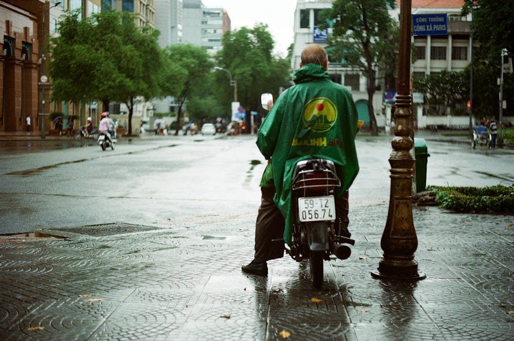 昼間の道路で赤いバイクに乗る緑のパーカーを着た男