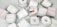 A collection of white candles, some with wooden wicks, arranged haphazardly on a flat surface. The candles are branded with 'French Candle Co' and have variations in size and shape. Some candles have lids with printed designs.