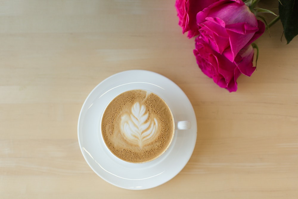white ceramic cup with cappuccino on white ceramic saucer beside pink rose