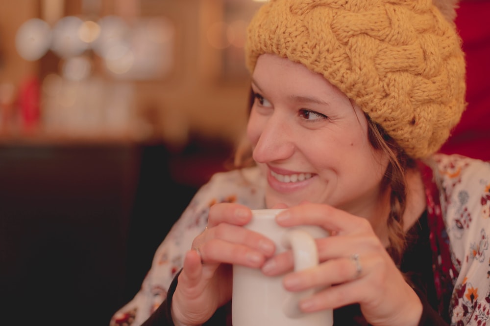 Mujer con gorro de punto marrón sosteniendo una taza de cerámica blanca