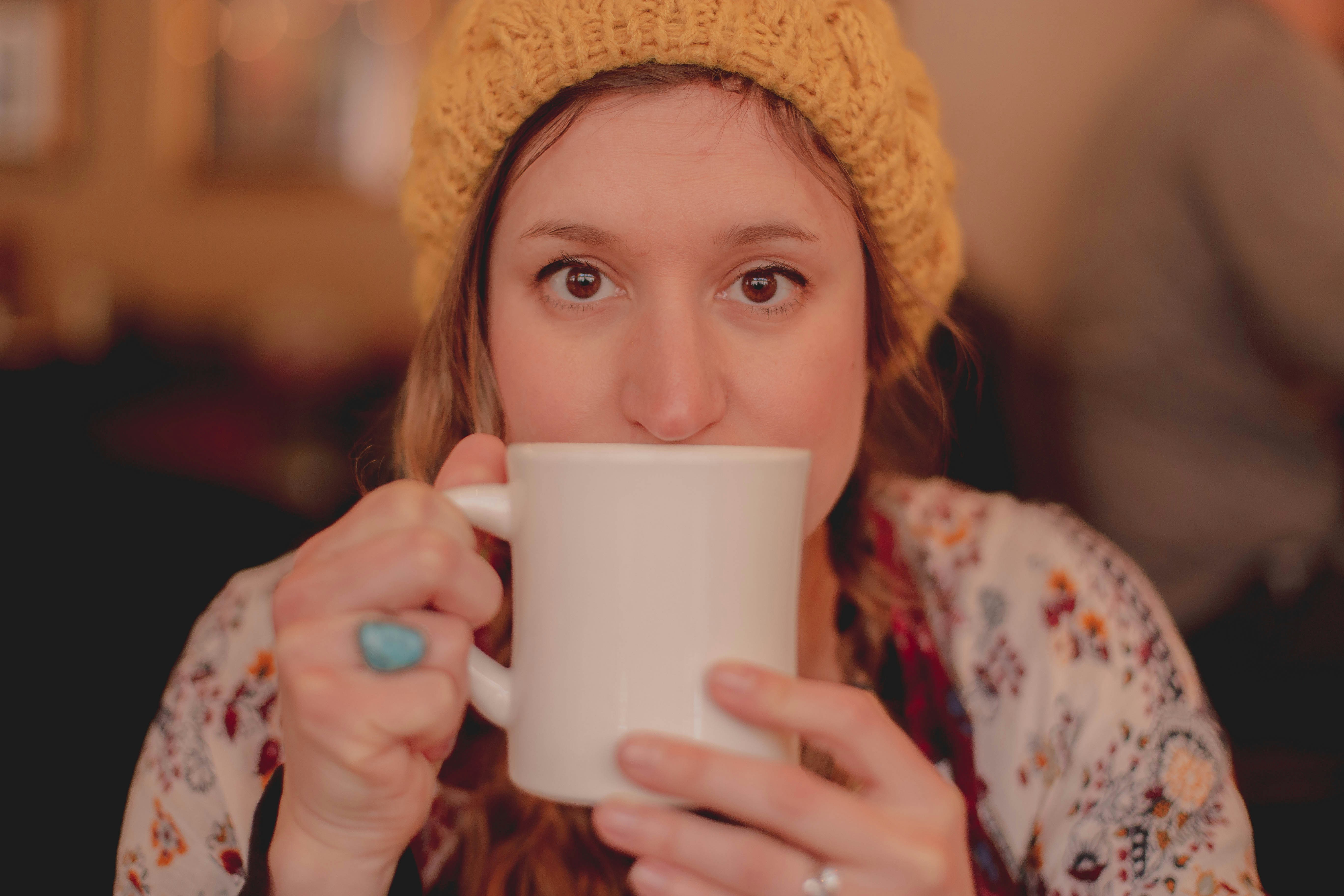 woman in beige knit cap holding white ceramic mug