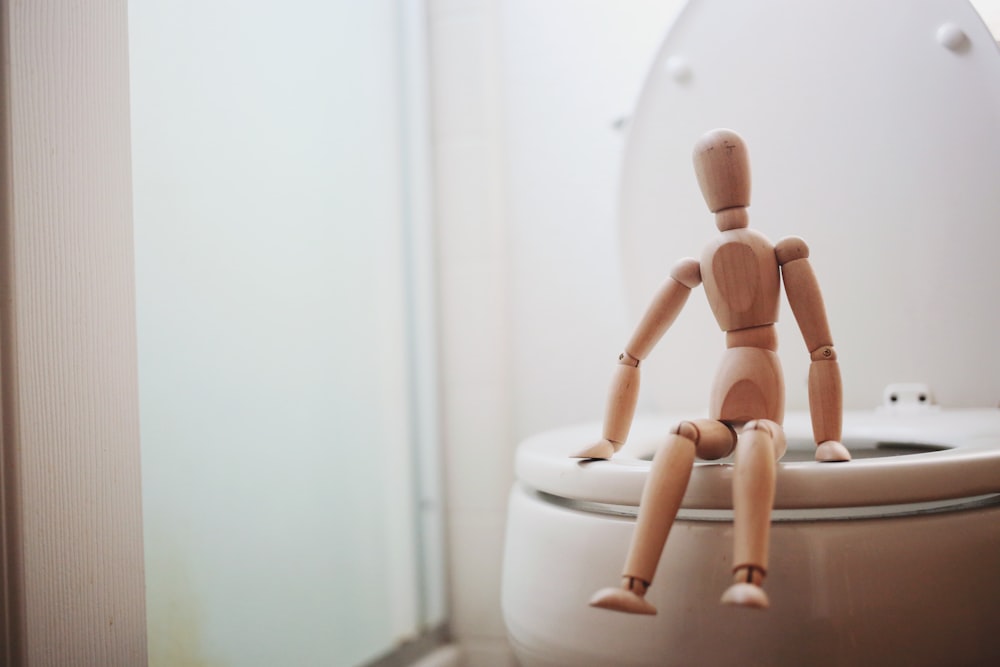poupée en bois marron sur cuvette de toilette en céramique blanche