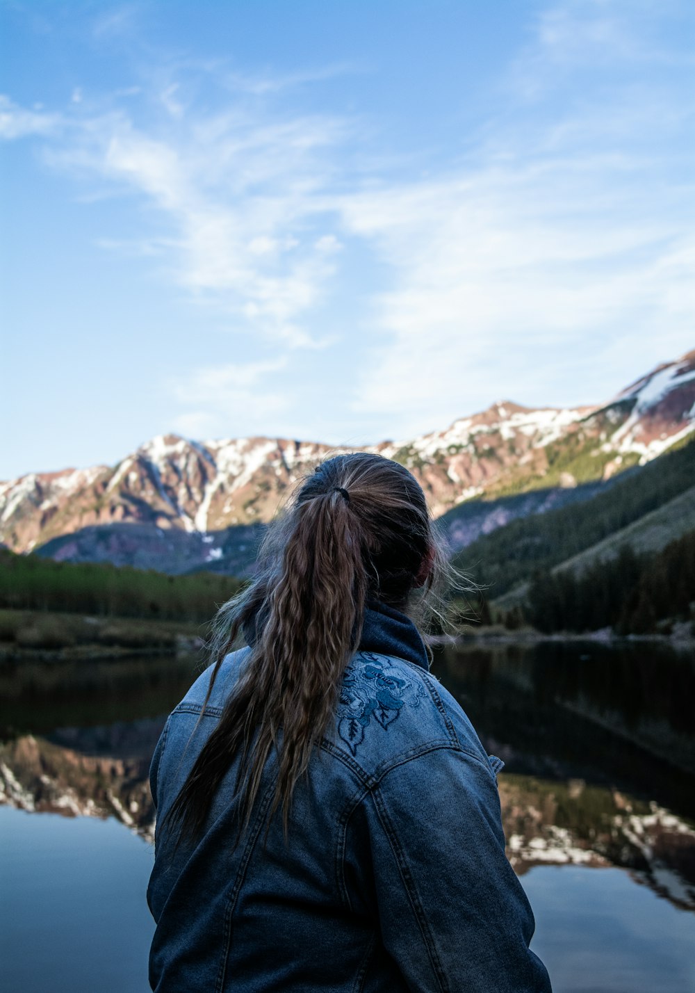 woman in blue denim jacket standing near lake during daytime