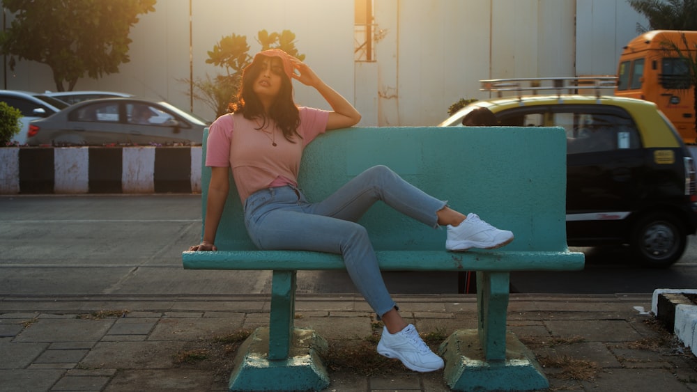 woman in pink shirt and blue denim jeans sitting on blue bench