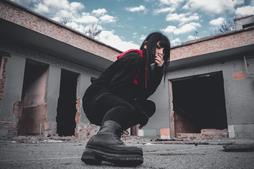 woman in black jacket and black pants sitting on gray concrete floor during daytime