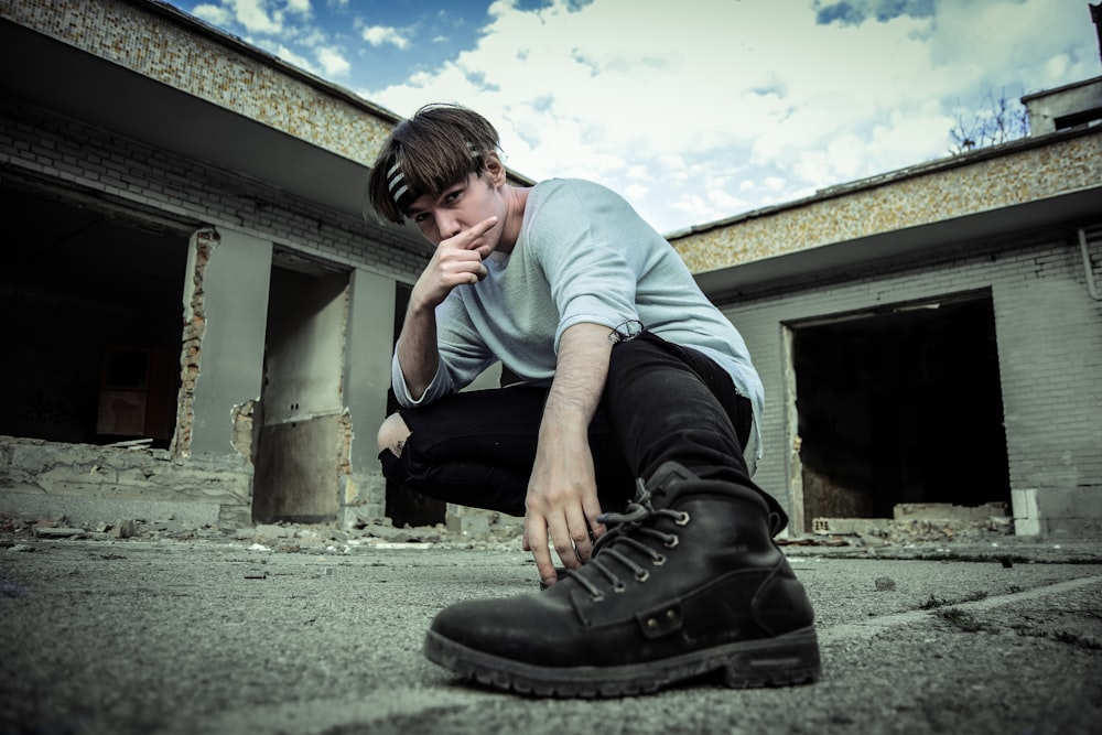 man in teal crew neck t-shirt and black pants sitting on concrete floor during daytime