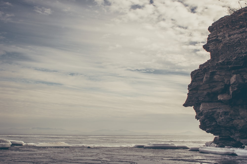 brown rock formation on sea under white clouds during daytime