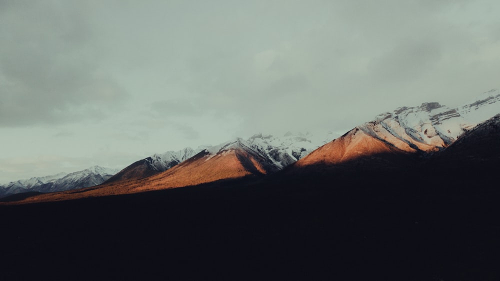 brown and white mountains under white clouds