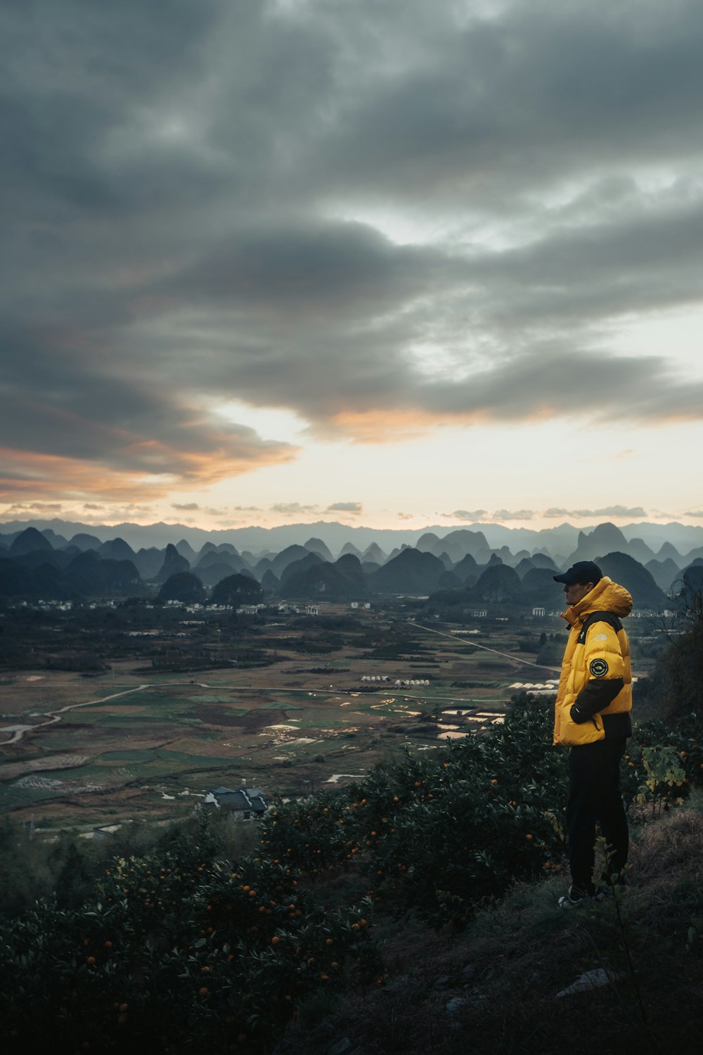 Femme en veste jaune et noire debout sur la formation rocheuse sous un ciel nuageux pendant la journée