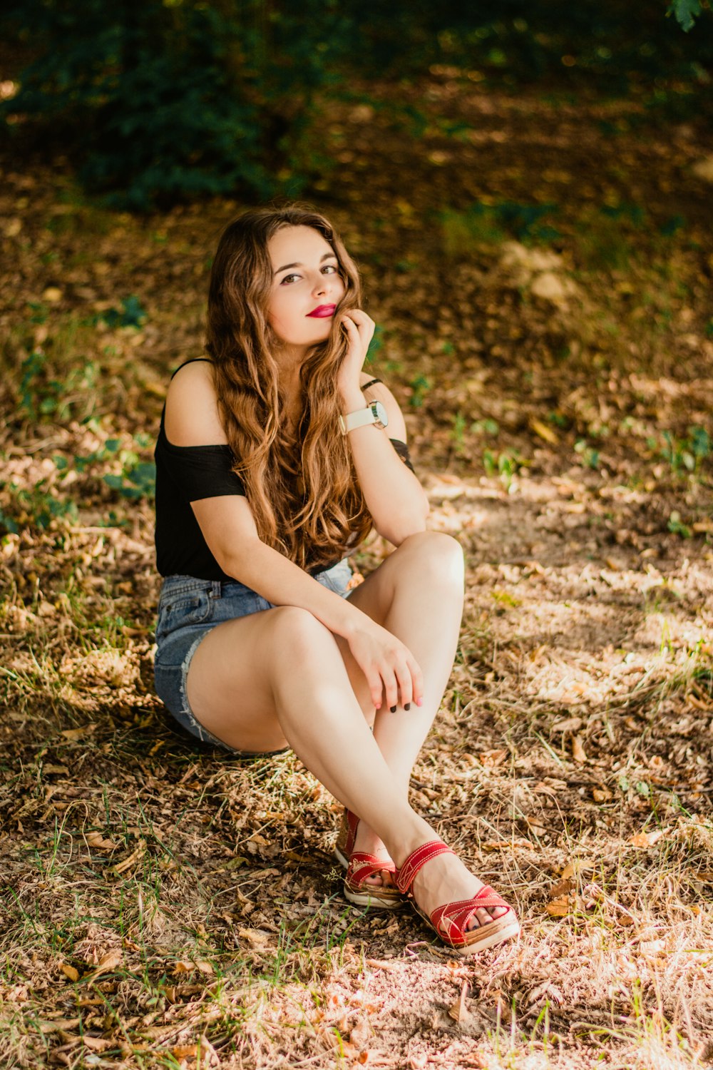 woman in black tank top and blue denim shorts sitting on brown grass during daytime