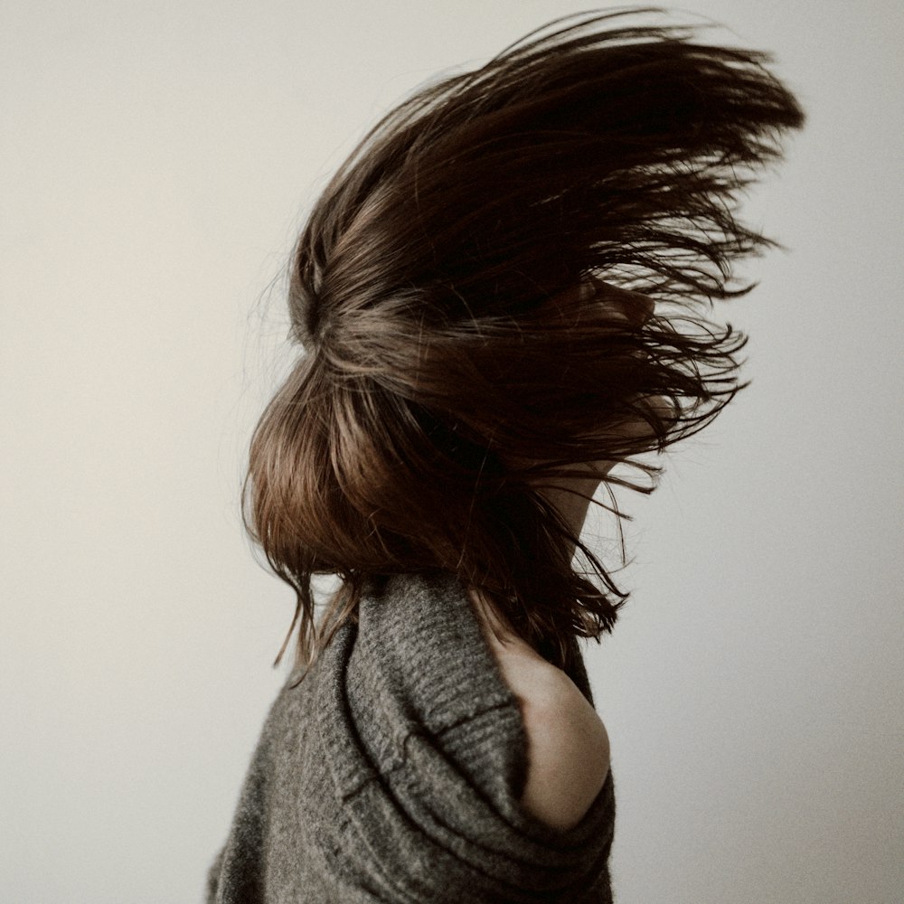 Mujer con suéter gris de pie cerca de la pared blanca