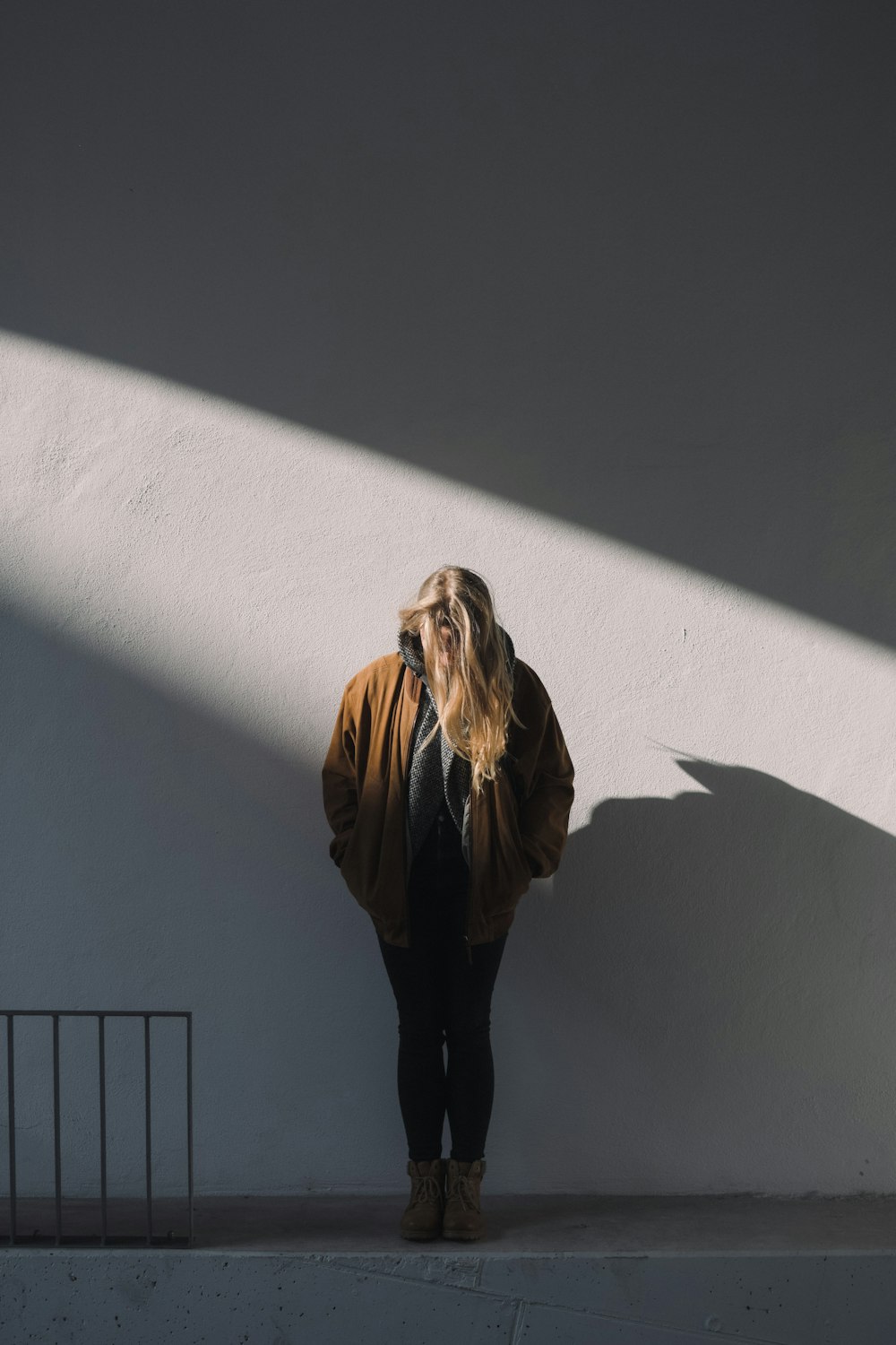 woman in brown jacket standing beside white wall