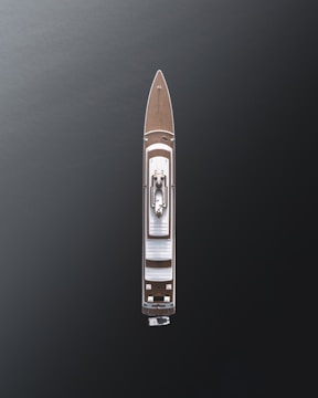 Aerial view of a large luxury yacht with a sleek design, positioned on dark, calm waters. The vessel features a wooden deck and a central structure, showcasing modern architecture with minimalistic details.
