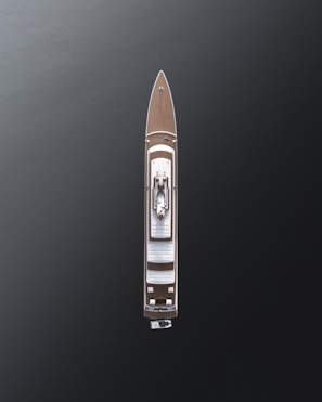 Aerial view of a large luxury yacht with a sleek design, positioned on dark, calm waters. The vessel features a wooden deck and a central structure, showcasing modern architecture with minimalistic details.