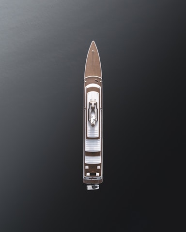 Aerial view of a large luxury yacht with a sleek design, positioned on dark, calm waters. The vessel features a wooden deck and a central structure, showcasing modern architecture with minimalistic details.