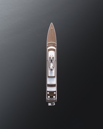 Aerial view of a large luxury yacht with a sleek design, positioned on dark, calm waters. The vessel features a wooden deck and a central structure, showcasing modern architecture with minimalistic details.