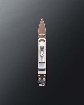 Aerial view of a large luxury yacht with a sleek design, positioned on dark, calm waters. The vessel features a wooden deck and a central structure, showcasing modern architecture with minimalistic details.