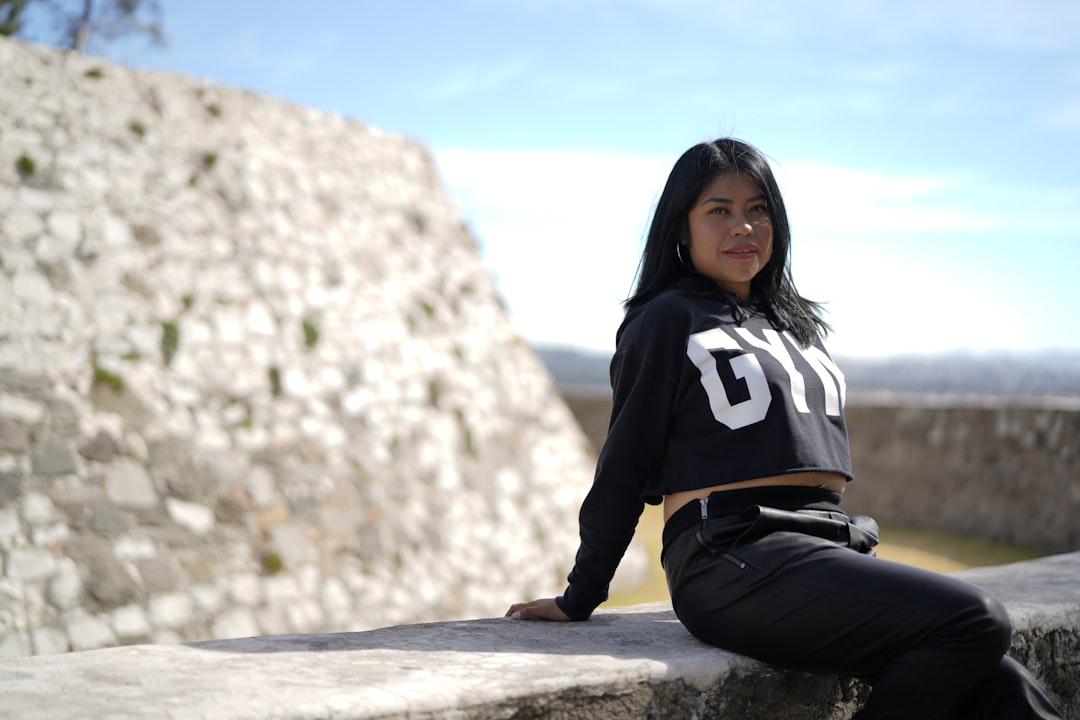 woman in black and white hoodie and black pants sitting on gray rock during daytime