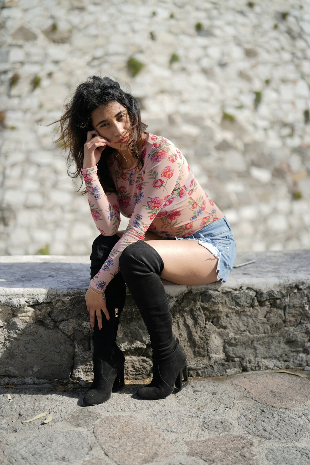 woman in pink and white floral long sleeve shirt and blue denim shorts sitting on gray