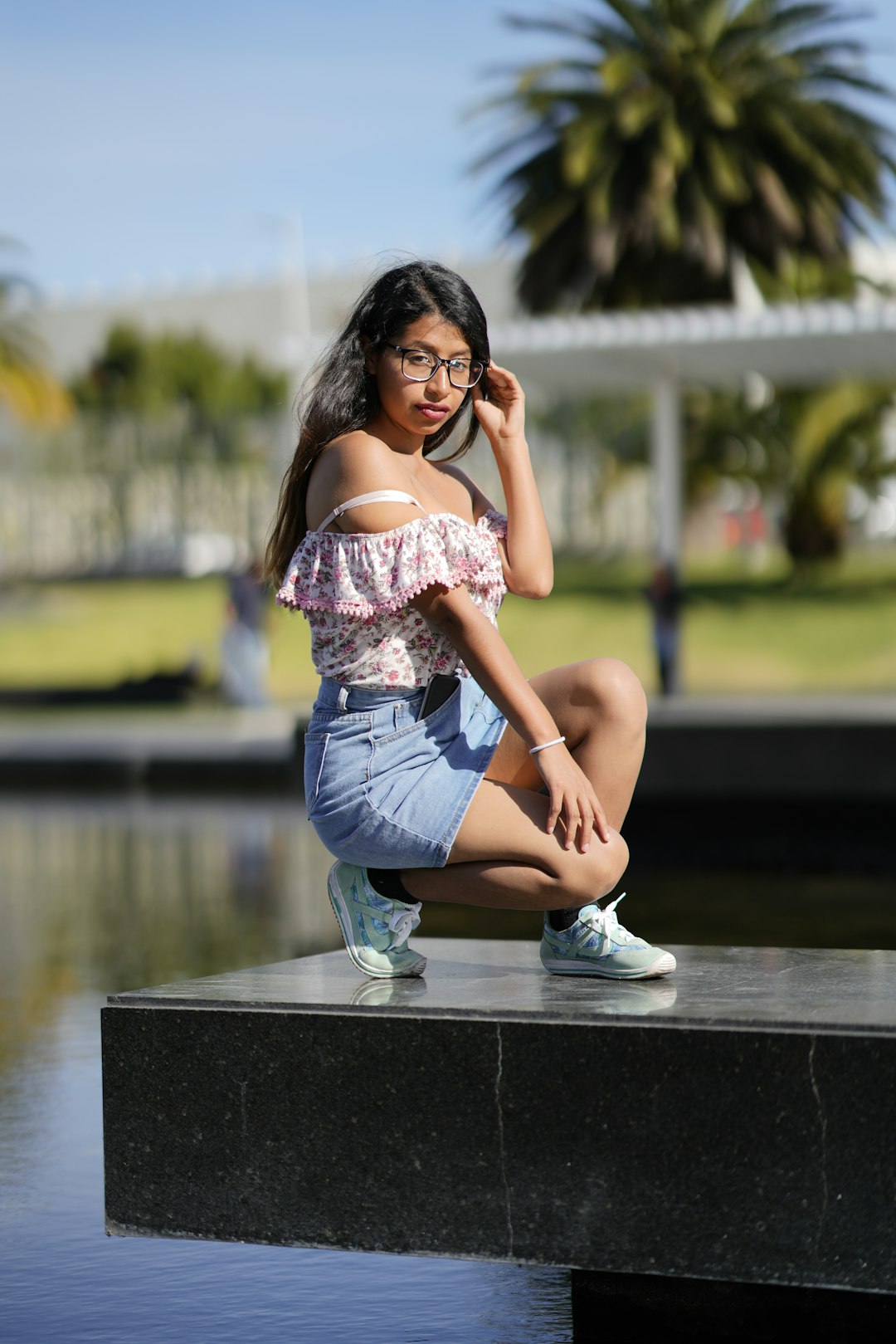 woman in white and pink floral tank top and blue denim shorts sitting on brown wooden