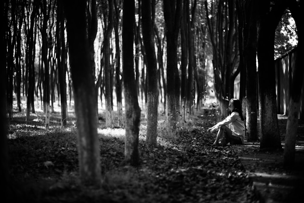 grayscale photo of man sitting on ground surrounded by trees
