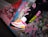 A person's legs wearing black leggings with colorful logos and bright, stylish sneakers. The sneakers are mainly white with pink and yellow accents and have a modern, sporty design. The background consists of a graffitied concrete surface, adding an urban and edgy feel.