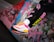 A person's legs wearing black leggings with colorful logos and bright, stylish sneakers. The sneakers are mainly white with pink and yellow accents and have a modern, sporty design. The background consists of a graffitied concrete surface, adding an urban and edgy feel.