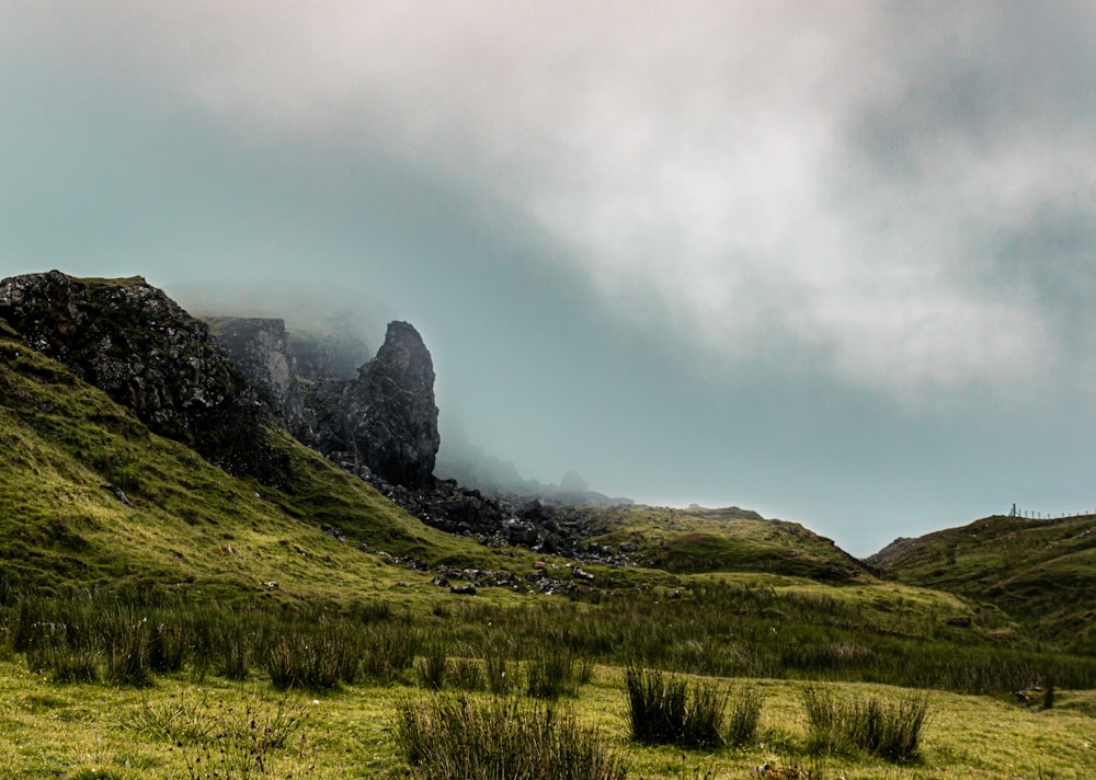 green grass field near mountain under cloudy sky during daytime