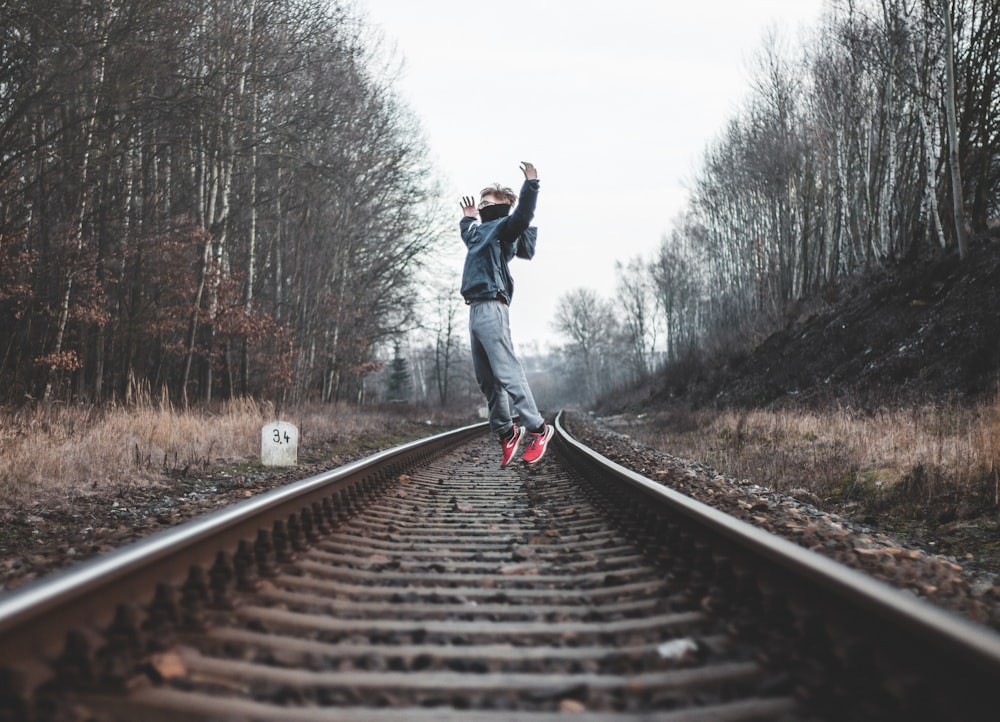 man in black jacket and blue denim jeans walking on train rail during daytime