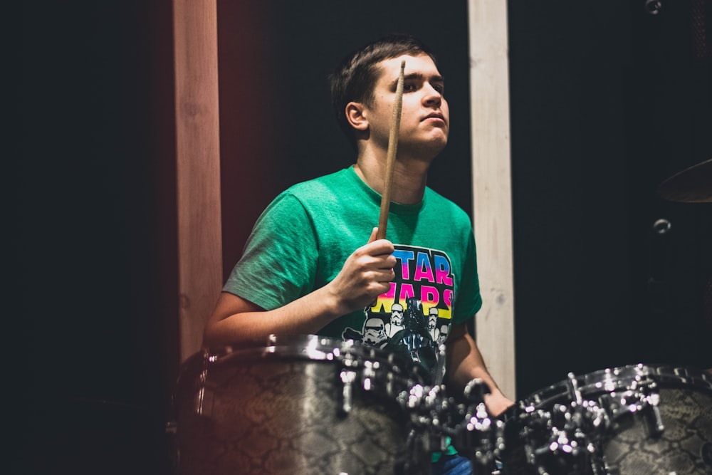 man in teal crew neck t-shirt playing drum