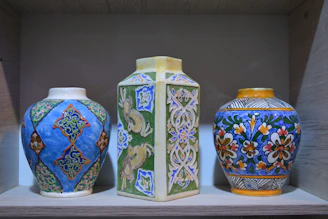 Handcrafted ceramic vase with intricate patterns displayed on a wooden shelf.