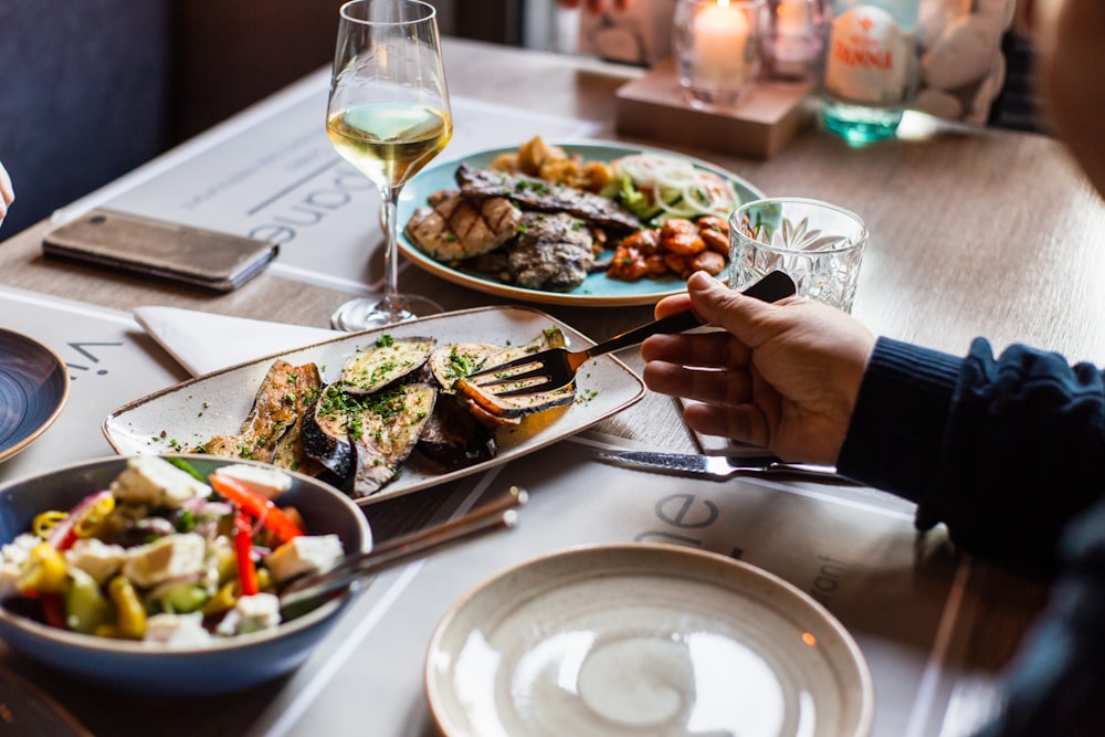 person holding fork and knife slicing vegetable on white ceramic plate