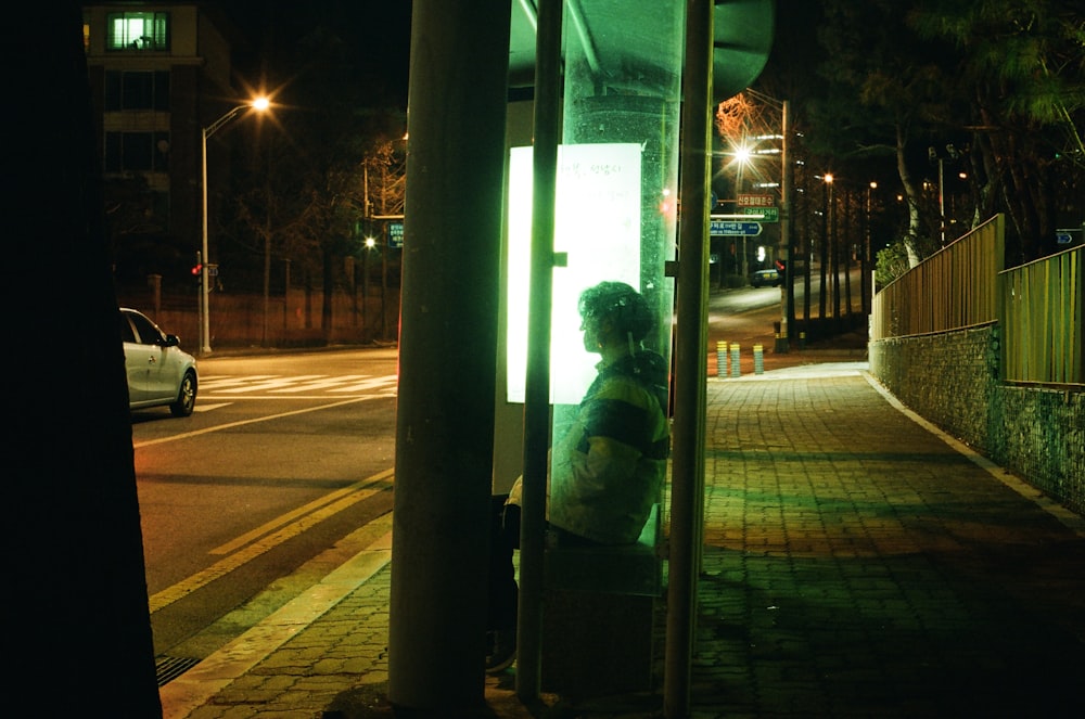 man in green and black jacket standing near glass wall during night time