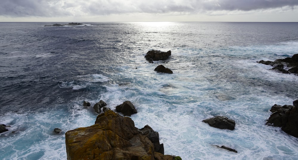 formação rochosa marrom no mar sob nuvens brancas durante o dia