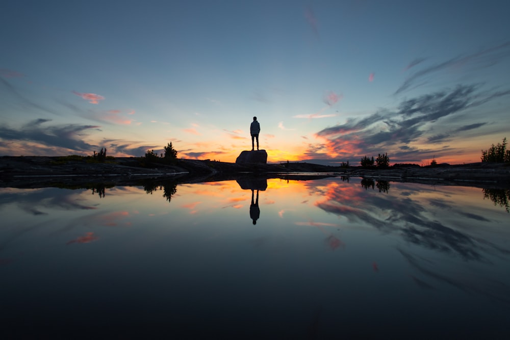 silhouette of man standing on dock during sunset