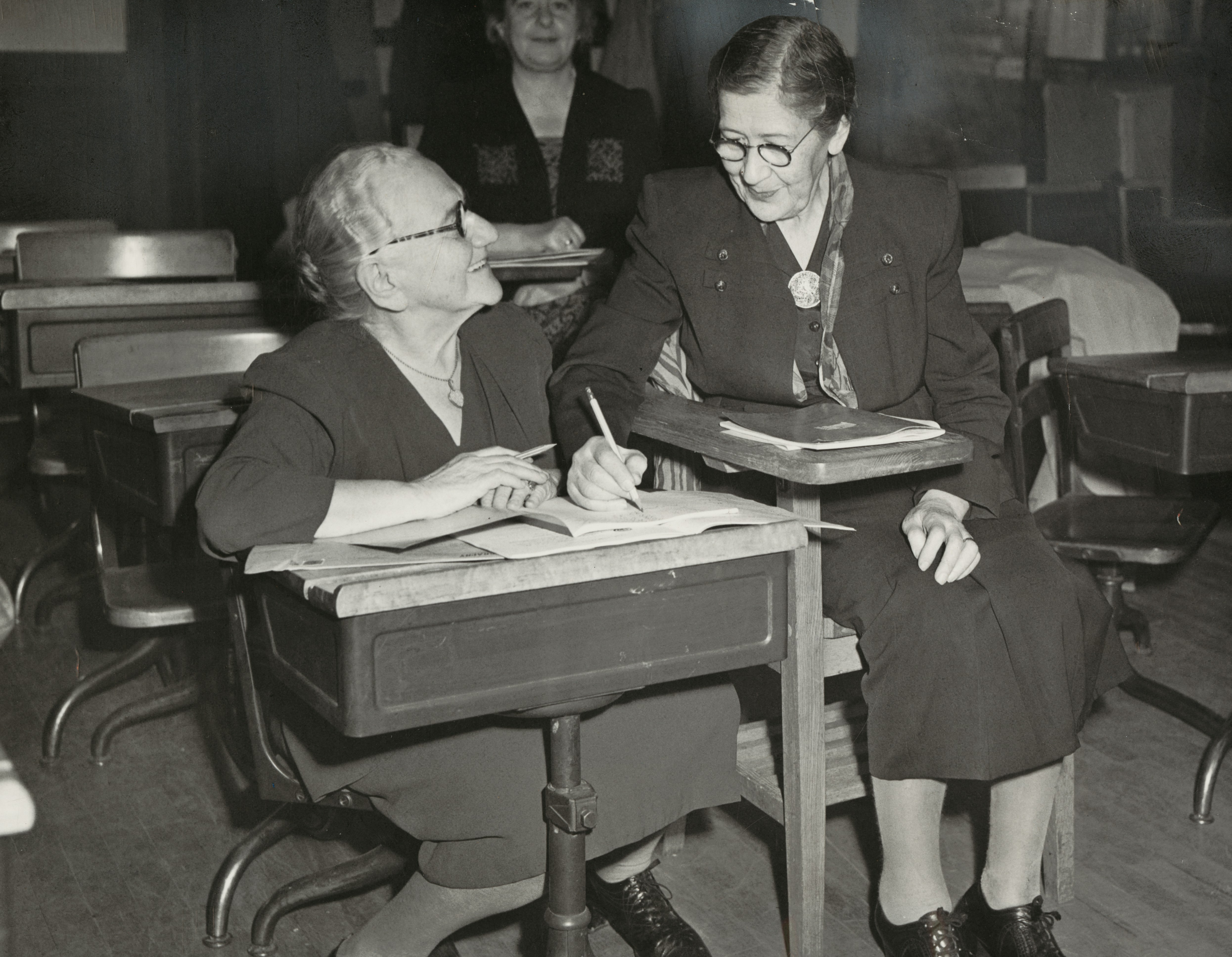 Age is no bar to studying when the pupils are working for their American citizenship. Mrs. Hedwig Gara, 76, at left, and Mrs. Rachel Alban, 84, help each other out in the school for DP's conducted by the Boston Section, National Council of Jewish Women, at Temple Kehillath Israel, Brookline. [from newspaper caption on recto] Published in the Boston Traveler on November 4, 1949. https://ark.digitalcommonwealth.org/ark:/50959/q524n565z Please visit Digital Commonwealth to view more images: https://www.digitalcommonwealth.org.