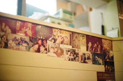 A wooden surface is adorned with numerous old photographs, showcasing various groups of smiling people. The images appear nostalgic and faded, offering glimpses of joyful gatherings, possibly in a social or family setting.