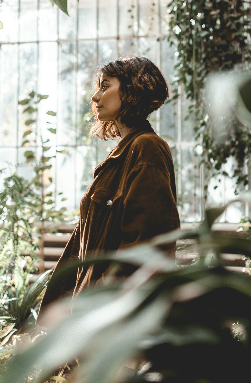woman in brown leather jacket standing near green plants during daytime