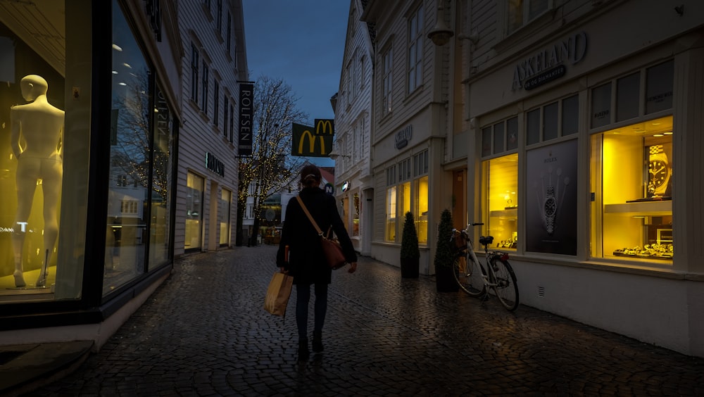 homme en veste noire marchant sur le trottoir pendant la nuit